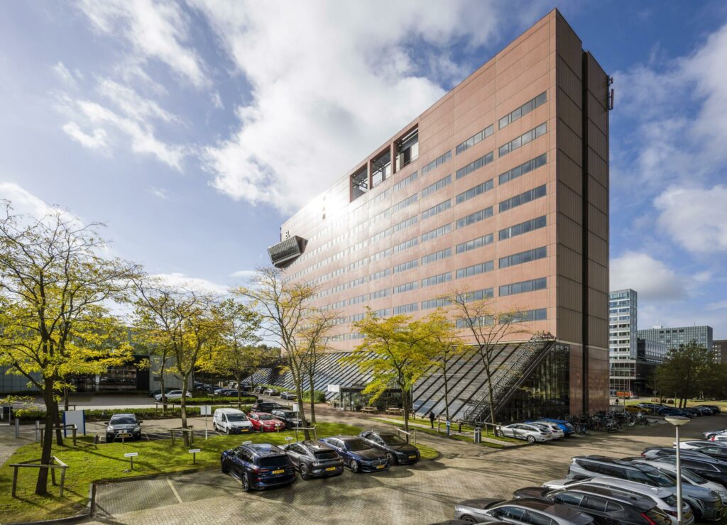 Kantoorgebouw aan de Johan Huizingalaan in Amsterdam met parkeerplaatsen en herfstbomen op de voorgrond.